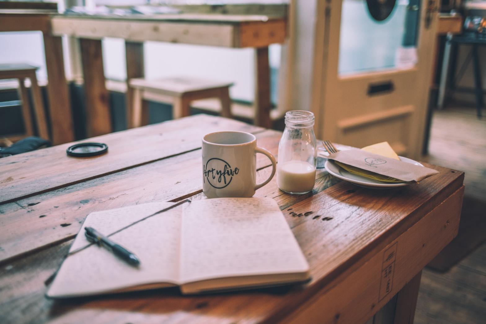 A journal, mug, bottle of milk, and plate on a table